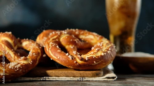 Oktoberfest food menu, soft pretzels and beer on wooden background. Beer is being poured. Misted glass with beer. Slow motion.