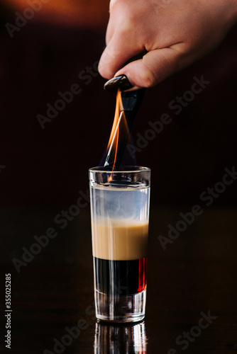 Close-up cocktail B52 on a bar, female hand sets fire to a drink