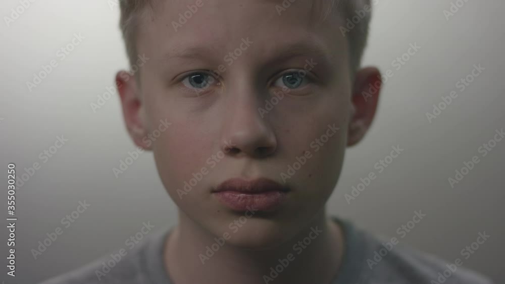 Closeup portrait of a young blonde caucasian boy in a grey tee with blue eyes looking right in camera with emotionless face expression Closeup portrait of a young blonde caucasian boy in a grey tee with blue eyes looking right in camera with emotionless face expression