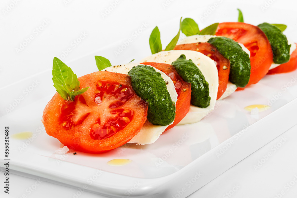 Tomato and mozzarella slices decorated with basil leaves on a plate and