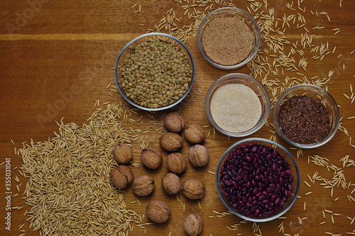 Top view of walnuts, seed, flax, beans, lentils and bran set in glass bowls as healthy dietary food on wooden board. Creative flatlay with cererals.