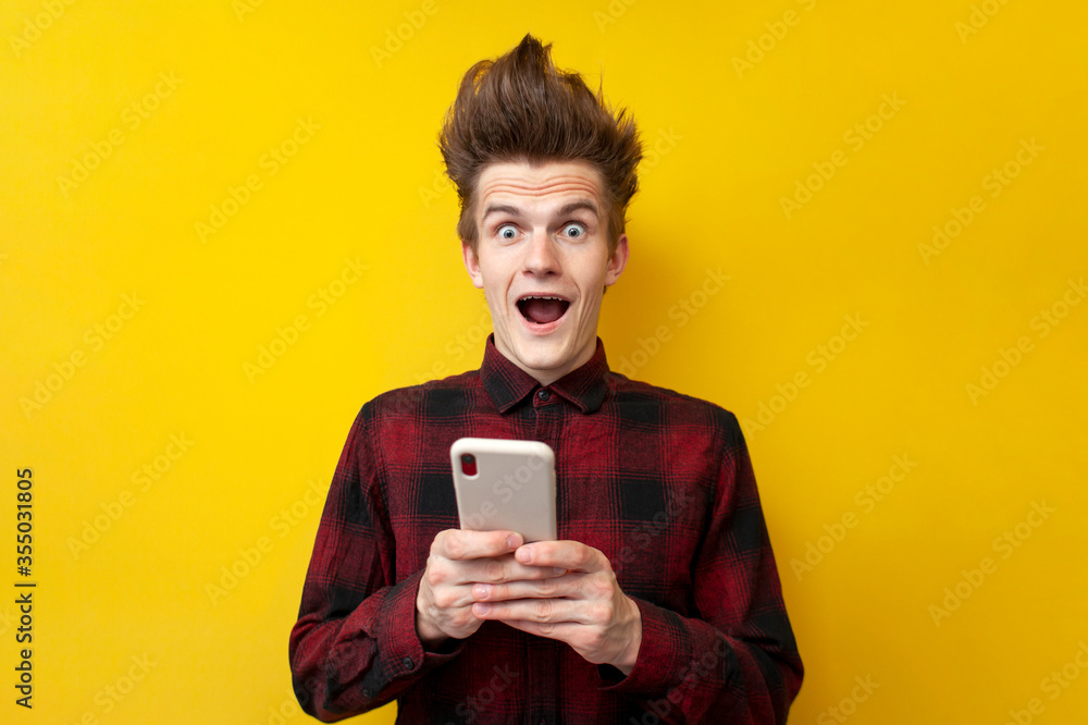 shocked guy with funny hairstyle use smartphone on yellow isolated background, hipster holds phone and is surprised shocked guy with funny hairstyle use smartphone on yellow isolated background, hipster holds phone and is surprised