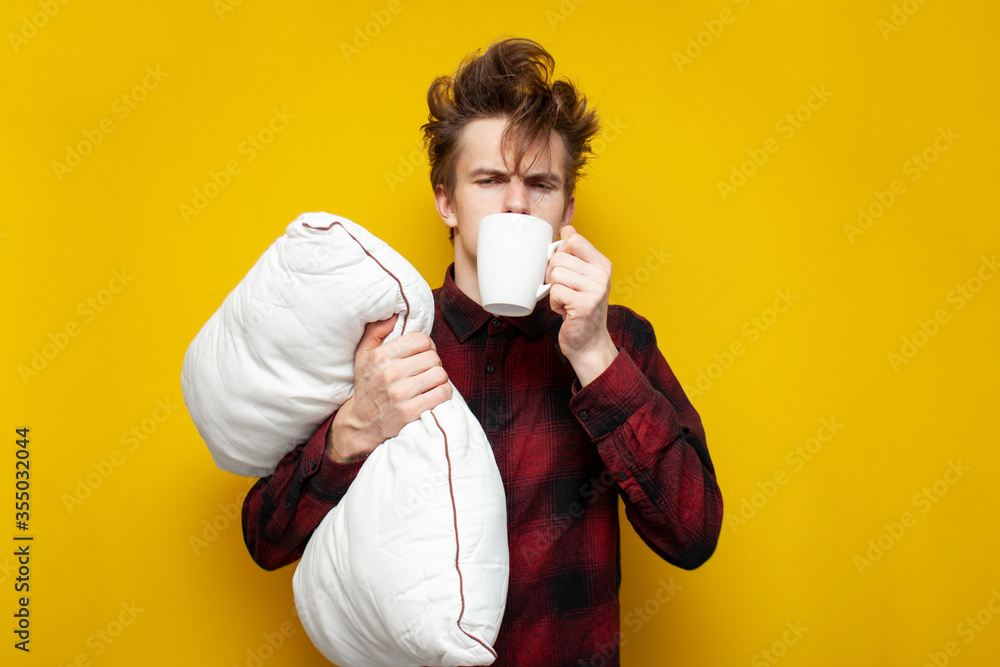 sleepy tired guy holds a pillow and drinks coffee in the morning on a yellow isolated background, bad morning, lack of sleep sleepy tired guy holds a pillow and drinks coffee in the morning on a yellow isolated background, bad morning, lack of sleep
