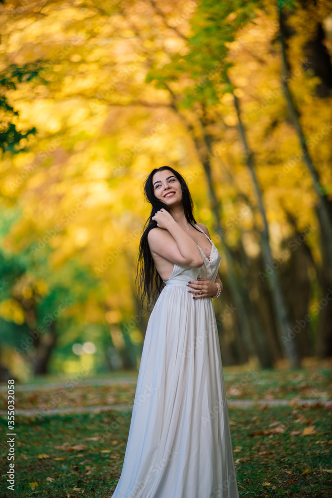 Young beautiful brunette female in a long white dress in autumn park. Young beautiful brunette female in a long white dress in autumn park.