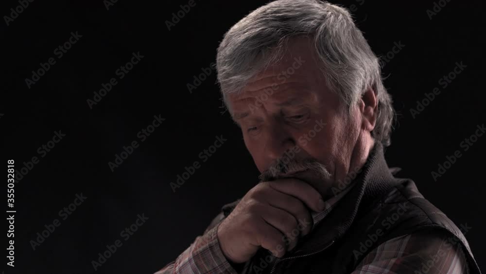 Thoughtful grey haired senior man looking down then on at camera and smile with camera slide out wearing jacket in semi lit light studio isolated on black background. Prores 422. Thoughtful grey haired senior man looking down then on at camera and smile with camera slide out wearing jacket in semi lit light studio isolated on black background. Prores 422.