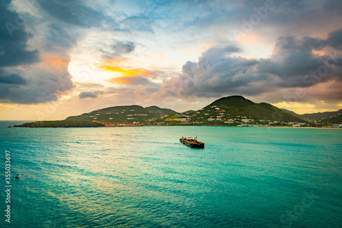 Sunset ocean view in the Caribbean with cruise ship fuel bunker vessel sailing to coast. Mountains stretch along the coastline landscape with endless water all around. photo