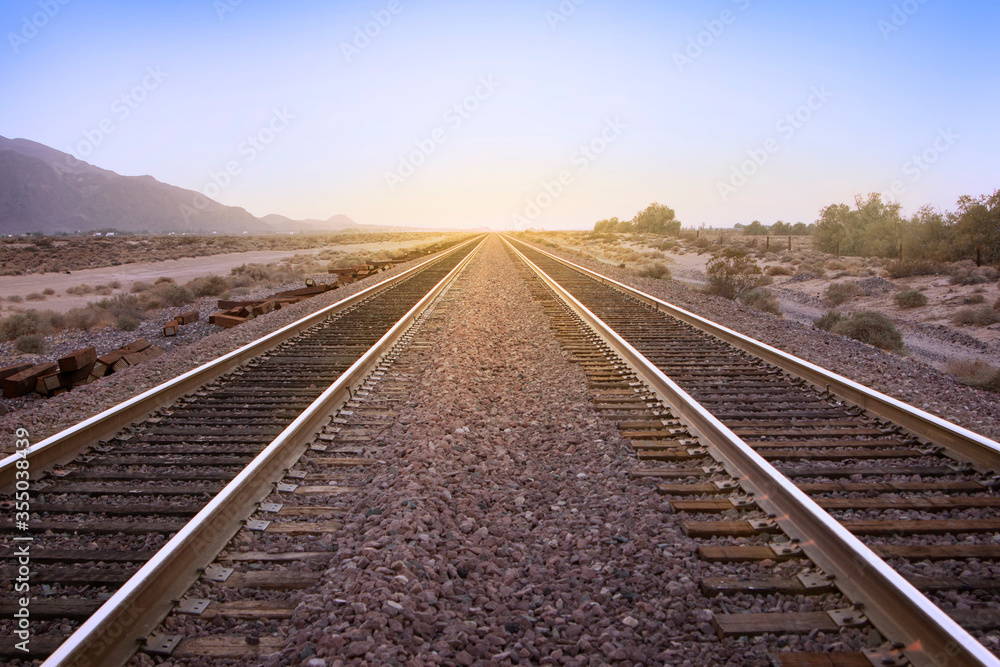 Two parallel rail road tracks vanishing on the horizon line and the golden setting sun