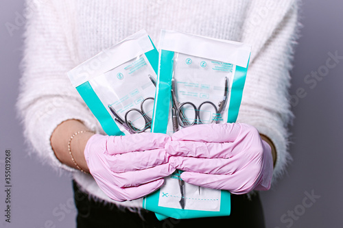Manicure set in the salon. Sterilization of instruments. Hands in pink gloves holding manicure tools 