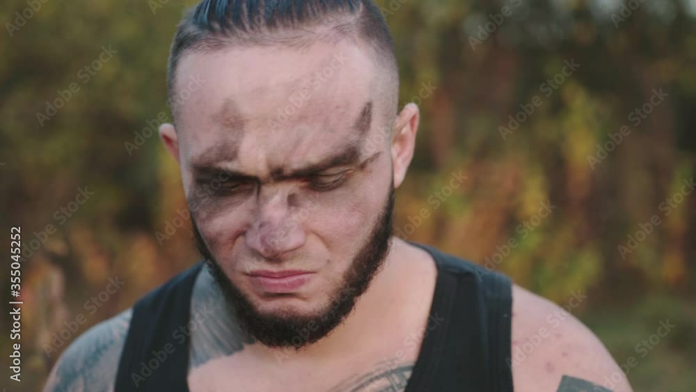 Brutal man with soot on face sharpening shavings and looking on it on nature Brutal man with soot on face sharpening shavings and looking on it on nature