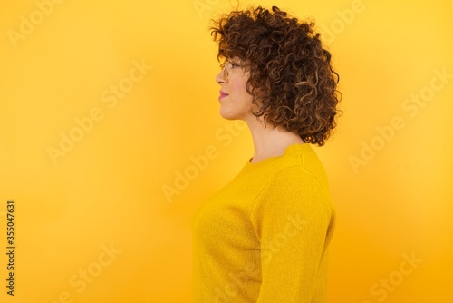 Young beautiful business woman with curly hair wearing yellow sweater looking to side, relax profile pose with natural face with confident smile.