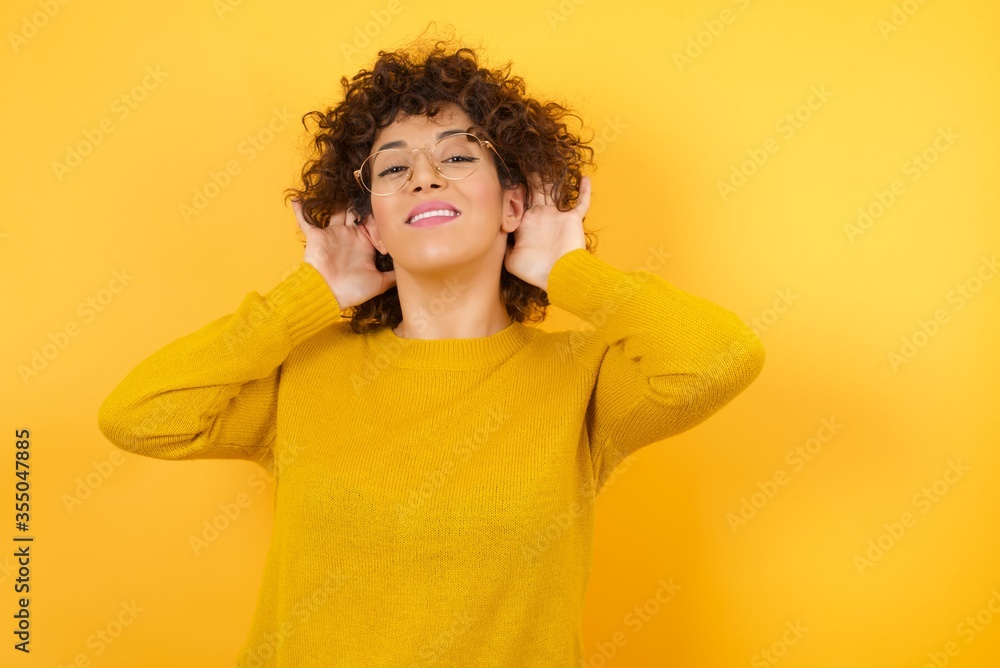 Young Arab woman wearing yellow sweater standing over isolated yelllow background Trying to hear both hands on ear gesture, curious for gossip. Hearing problem, deaf Young Arab woman wearing yellow sweater standing over isolated yelllow background Trying to hear both hands on ear gesture, curious for gossip. Hearing problem, deaf