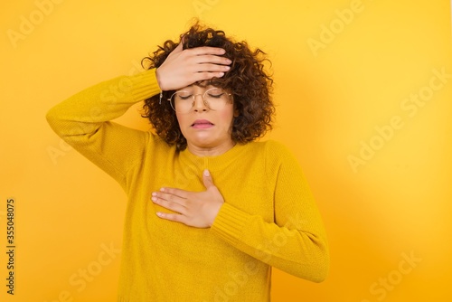 Young beautiful woman wearing casual yellow sweater and glasses over isolated white background Touching forehead for illness and fever, flu and cold, virus sick. © Roquillo