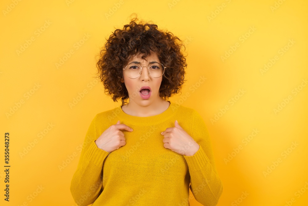 Photo of embarrassed Arab female indicates at herself with puzzled expression, being shocked to be chosen to participate in competition, hesitates about something isolated on white wall Photo of embarrassed Arab female indicates at herself with puzzled expression, being shocked to be chosen to participate in competition, hesitates about something isolated on white wall