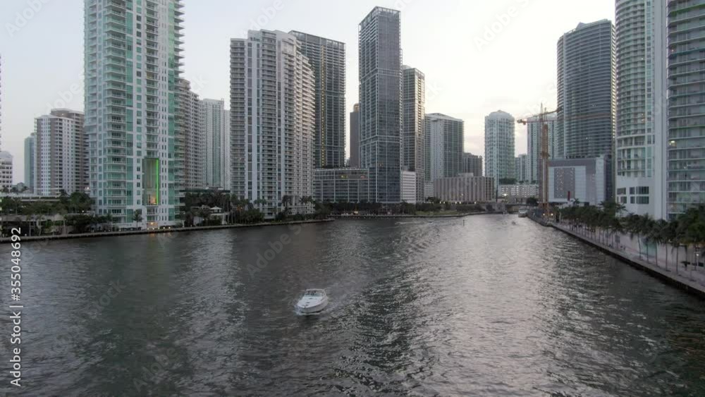 Aerial shot of boat in canal against skyscrapers during sunset, drone flying backward from buildings in city against sky - Miami, Florida Aerial shot of boat in canal against skyscrapers during sunset, drone flying backward from buildings in city against sky - Miami, Florida