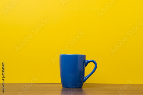 Blue coffee cup on yellow background with copy space.