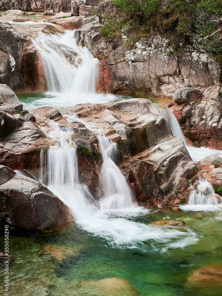Fototapeta premium Waterfall of Mata de Albergaria in the middle of the woods the water runs down the rocks until de green lake