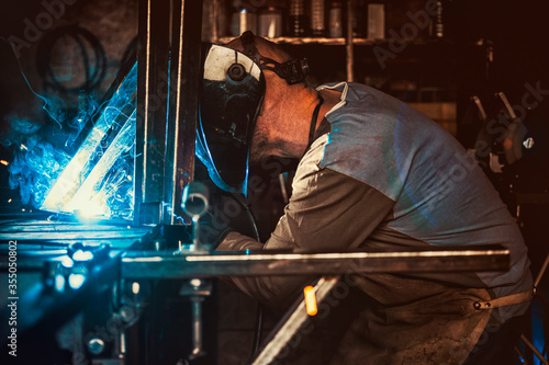 Welder working in the workshop. Welding a metal construction. Sparkles and combustion. Hard work.