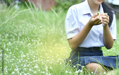 Young student girl sitting on grasses and holding grasses flowers on hand. Young people enjoyment with beautiful meadow nature in garden after break from study hour. 