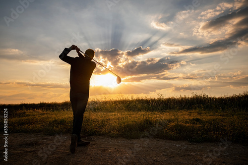 Jugador de golf  jugando al golf al atardecer, con el sol de frente y nubes en el cielo photo