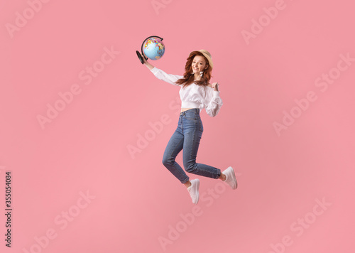 Happy Traveler Girl Jumping Holding Globe Gesturing Yes, Pink Background