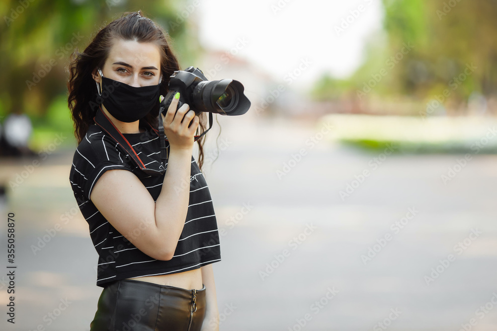 beautiful girl with a camera wears a medical mask and takes pictures in the park. Coronavirus 2019 nCoV pneumonia outbreak beautiful girl with a camera wears a medical mask and takes pictures in the park. Coronavirus 2019 nCoV pneumonia outbreak