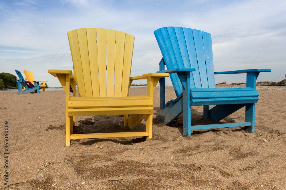a blue and a yellow adirondack wooden beach chairs together on a sandy beach