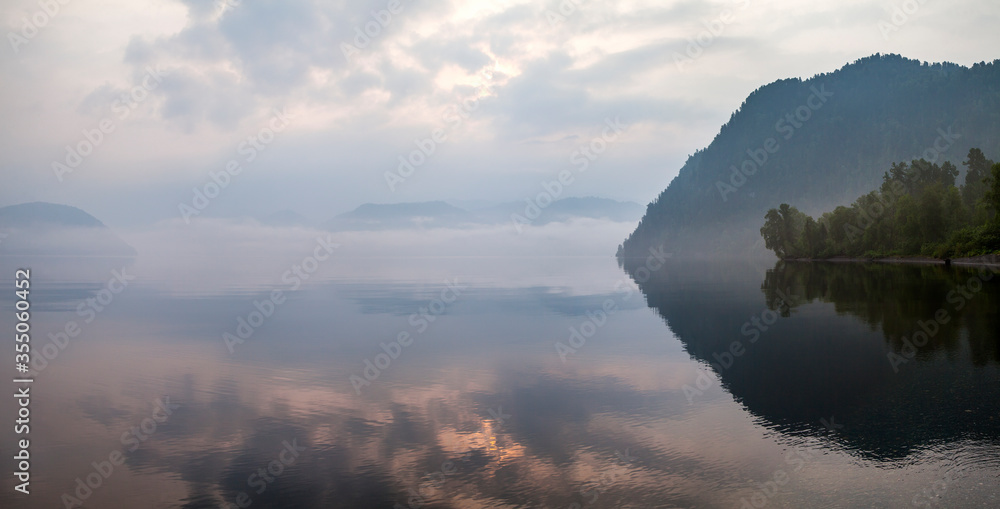 Picturesque mountain lake. Sunset sky is reflected in the water, fog. Natural light.