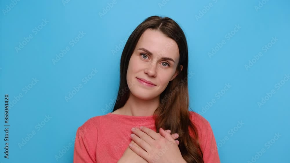 Cheerful positive young woman with lovely sincere smile feeling thankful and grateful, showing her heart filled with love and gratitude holding hands on her breast, isolated on blue studio background Cheerful positive young woman with lovely sincere smile feeling thankful and grateful, showing her heart filled with love and gratitude holding hands on her breast, isolated on blue studio background