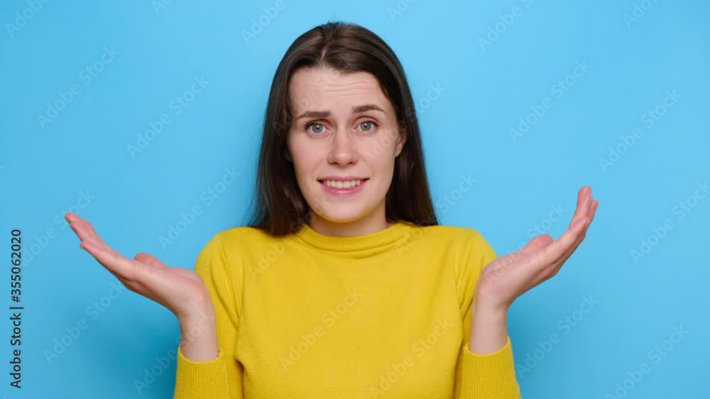 Portrait of brunette woman with puzzled expression, spreads hands with confused look, frowns face, feels hesitant, indignant, wears yellow sweater, isolated over blue studio background. Doubt concept Portrait of brunette woman with puzzled expression, spreads hands with confused look, frowns face, feels hesitant, indignant, wears yellow sweater, isolated over blue studio background. Doubt concept