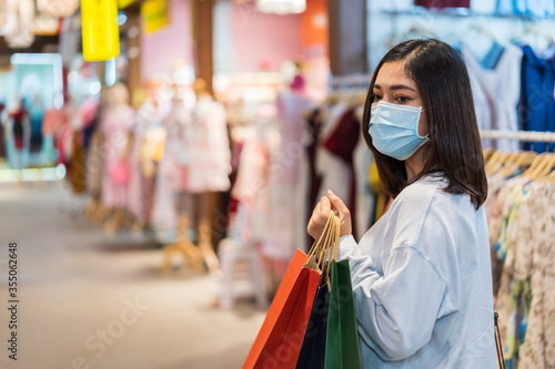 woman holding shopping bag and looking to clothes at mall and her wearing medical mask for prevention from coronavirus (Covid-19) pandemic. new normal concepts