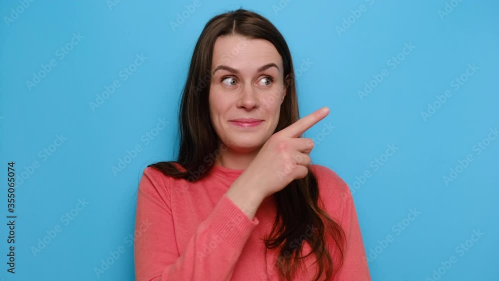 Portrait of positive glad young woman with has amazed expression, indicates a blank copy space for your advertisment or promotional content, wears red sweater, poses against blue studio background Portrait of positive glad young woman with has amazed expression, indicates a blank copy space for your advertisment or promotional content, wears red sweater, poses against blue studio background