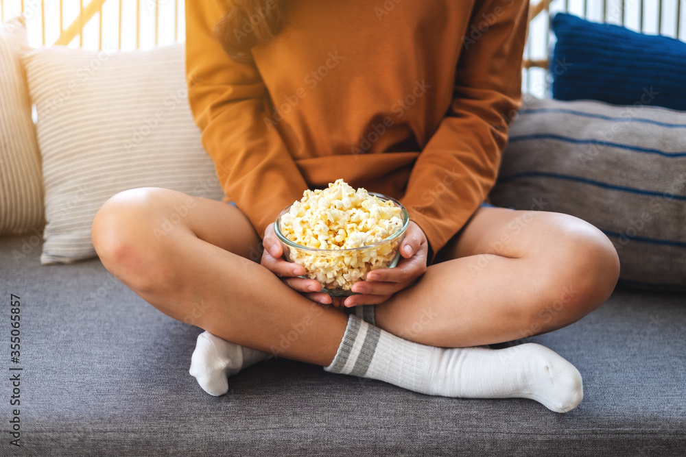 Close up image of a woman holding a bowl of pop corn while sitting on sofa at home Close up image of a woman holding a bowl of pop corn while sitting on sofa at home