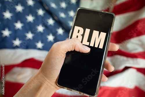 Hand holding a cellphone with the abbreviation of Black Lives Matter against the US flag photo