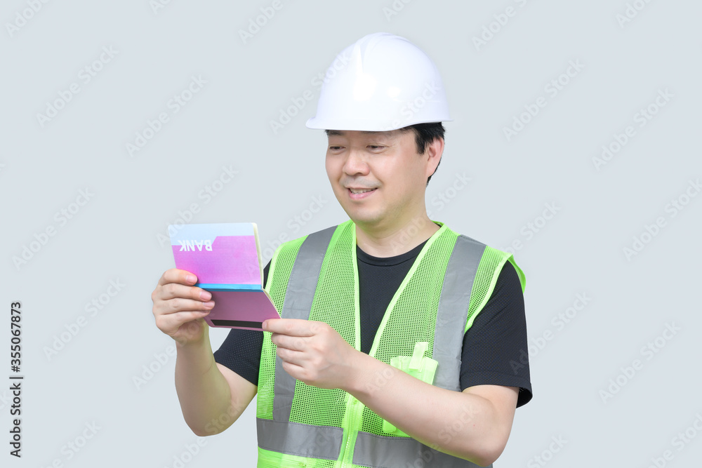 A middle-aged Asian engineer holding a bank passbook in his hand on a gray background. A middle-aged Asian engineer holding a bank passbook in his hand on a gray background.