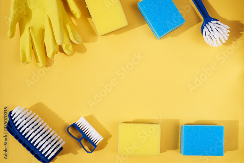Blue dish brushes and yellow gloves and sponge on a yellow background. Space for text