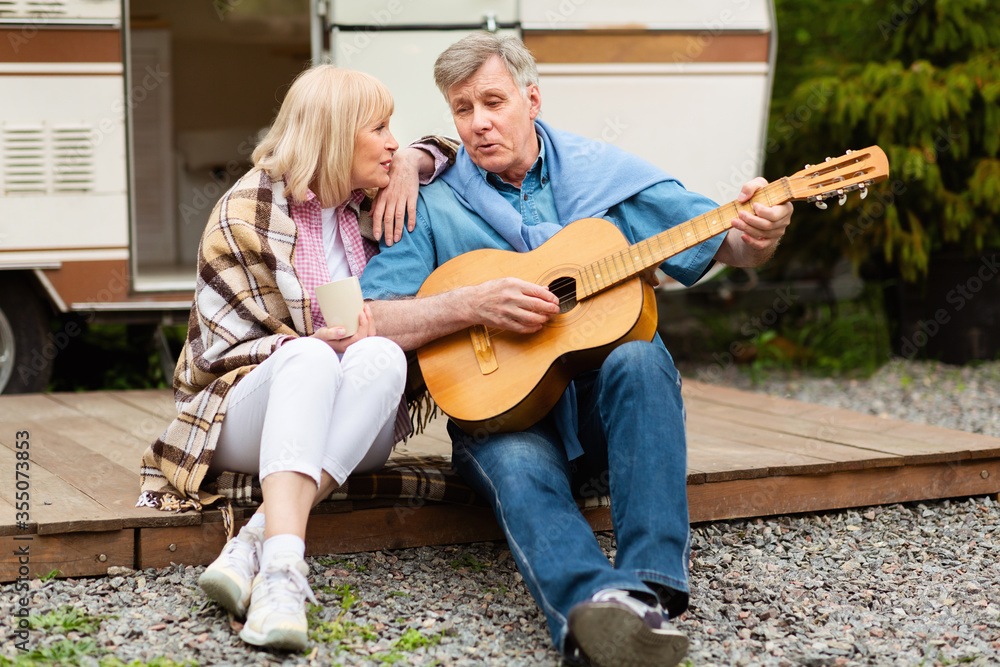 Retired couple with guitar singing together near their motorhome at campsite