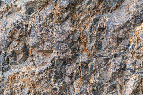 Rock formation for backdrop. Sulphide ore interspersed with copper-nickel. Black and rusty streaks. Uneven surface.