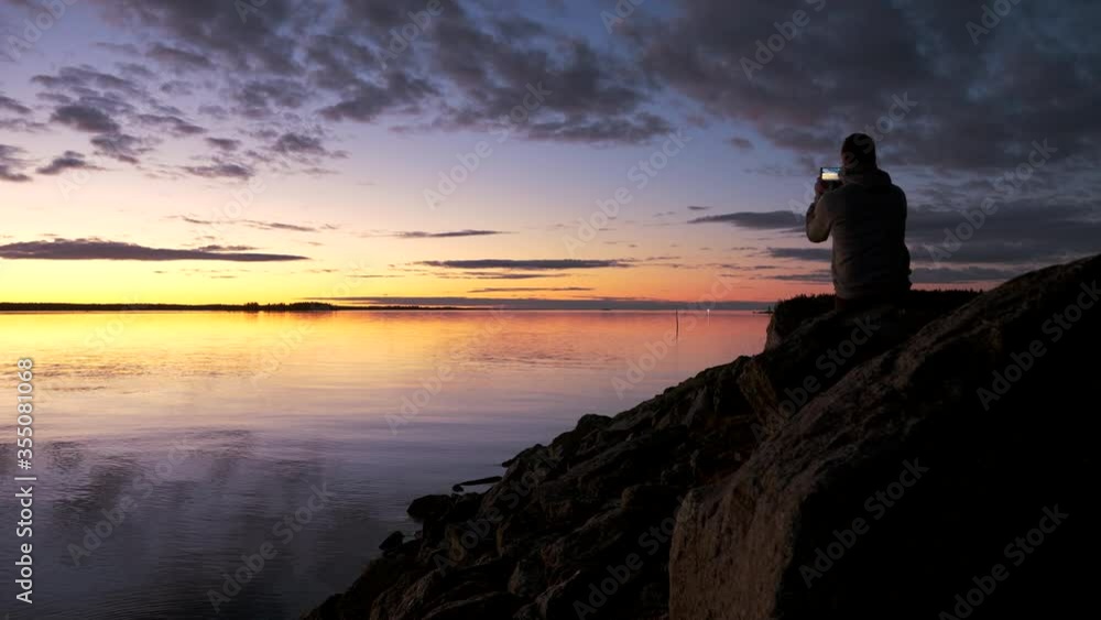 Man Using the Mobile to Capturing Color Sunset in Kvarken Archipelago Man Using the Mobile to Capturing Color Sunset in Kvarken Archipelago