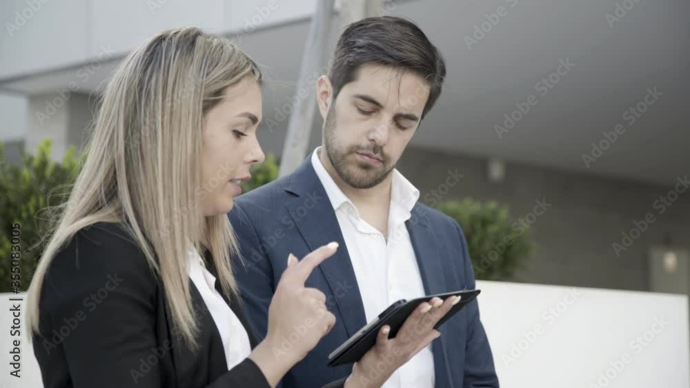 Focused business couple using tablet outdoors, discussing project, watching presentation. Medium shot, front view. Communication concept Focused business couple using tablet outdoors, discussing project, watching presentation. Medium shot, front view. Communication concept