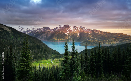 Glacial mountain Garibaldi lake with turquoise water in the middle of coniferous forest at sunset. View of a mountain lake between fir trees. Mountain peaks above the lake lit by sunset rays. Canada photo