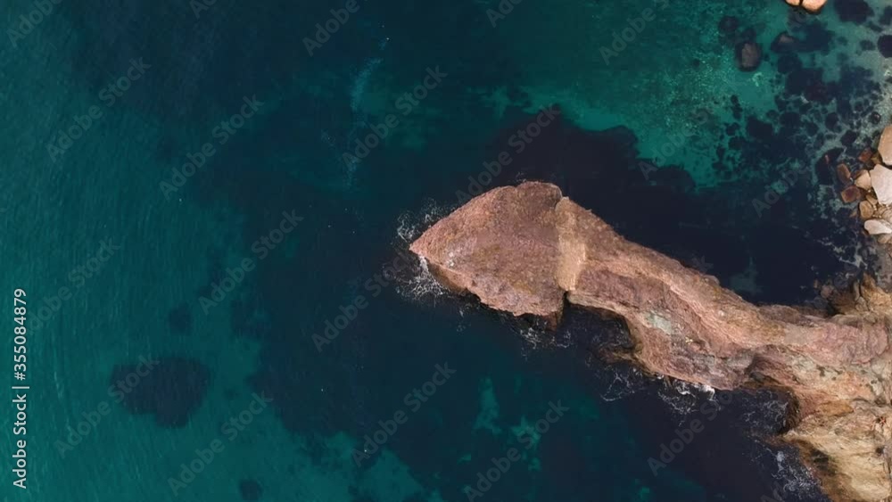 The view from the bird's eye view on the steep coast with crystal clear turquoise sea, waves breaking on the rocks and cliffs. Blue ocean waves. The view from the bird's eye view on the steep coast with crystal clear turquoise sea, waves breaking on the rocks and cliffs. Blue ocean waves.