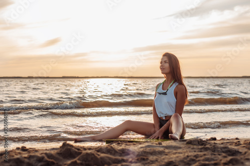Young caucasian woman surfer in white shirt sitting on her surfboard on the beach