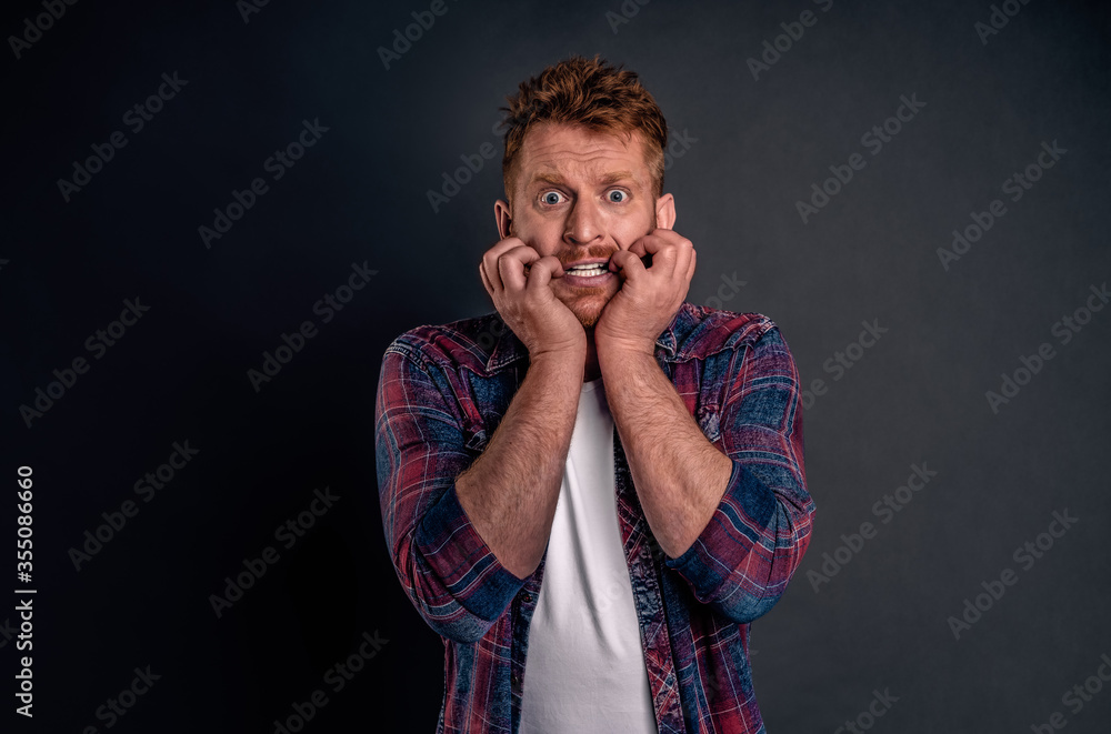 Man feeling worried for car seeing wife driving it careless. Nervous good-looking redhead guy with bristle, biting fingernails and staring anxious and shook at camera, feeling scared over gray wall Man feeling worried for car seeing wife driving it careless. Nervous good-looking redhead guy with bristle, biting fingernails and staring anxious and shook at camera, feeling scared over gray wall