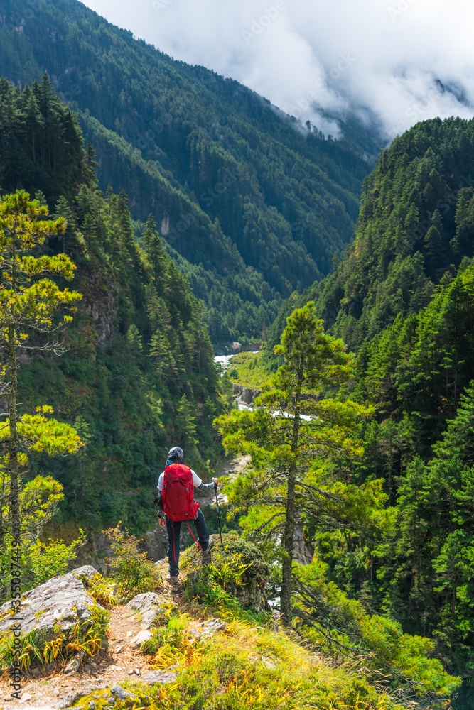 A man trekker with backpack standing up on hill and looking to mountain valley, Himalaya mountains range in Everest base camp trekking route, Nepal