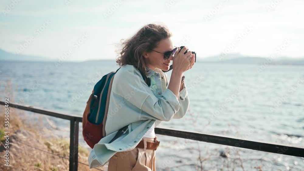 Happy young woman takes a picture on a photo camera walking sea, summer travel. High quality 4k footage