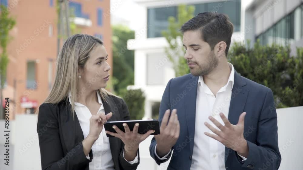 Happy business couple using tablet outdoors, discussing project. Medium shot, front view. Communication and teamwork concept Happy business couple using tablet outdoors, discussing project. Medium shot, front view. Communication and teamwork concept