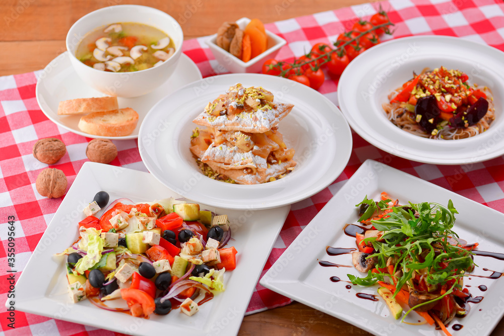 Different food, Italian dishes on the table. Vegetable and meat salad, pasta, soup and puff pastry dessert.