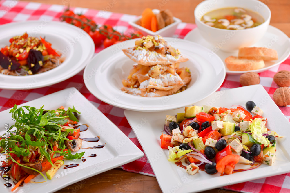 Different food, Italian dishes on the table. Vegetable and meat salad, pasta, soup and puff pastry dessert.