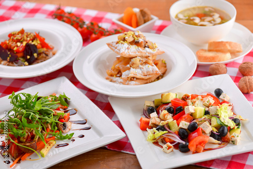 Different food  Italian dishes on the table. Vegetable and meat salad  pasta  soup and puff pastry dessert.