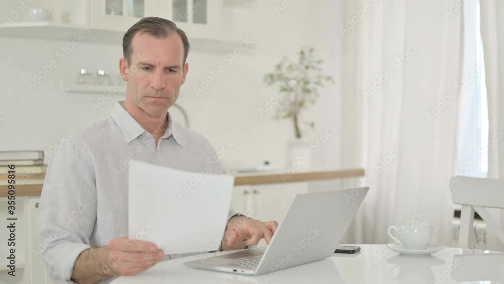 Focused Middle Aged Man working on Laptop and Document at Home Focused Middle Aged Man working on Laptop and Document at Home